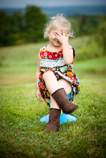 A vertical shallow focus shot of a cute small girl sitting on a chair and covering her face in a field
