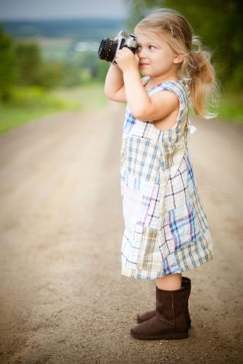 A vertical shallow focus shot of a cute blonde small girl taking pictures in the countryside