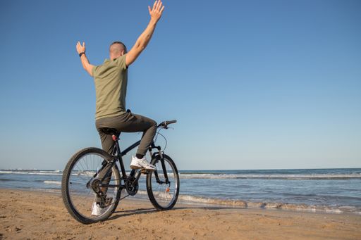 A male riding a bike on the coast of a lake with his hands up