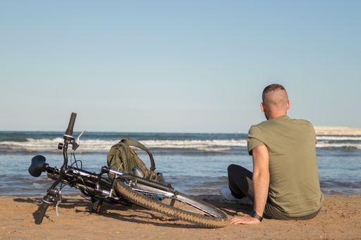 A back view of a male sitting on the coast of a lake near his bike