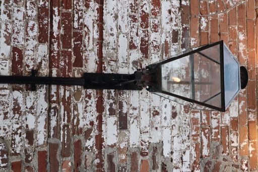 A vertical closeup of the metal gaslamp fixture on the red and white brick wall.