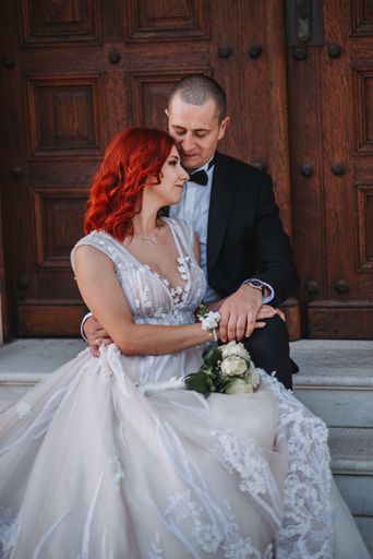 A vertical shot of a groom and a bride with red hair holding each other, posing for the camera