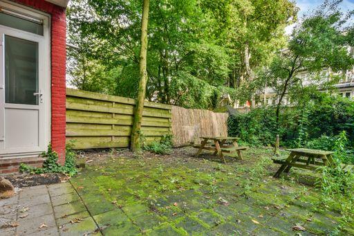 A closeup shot of a small yard of a building with wooden benches and tables among trees