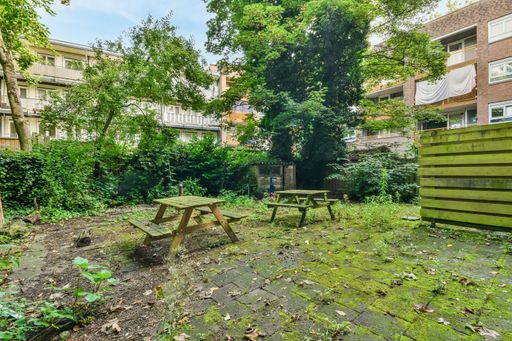 A closeup shot of a small yard of a building with wooden benches and tables among trees