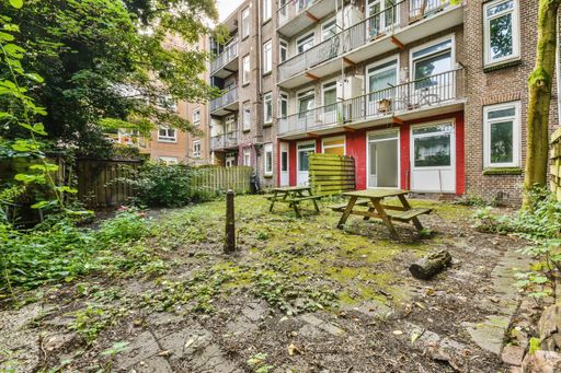 A closeup shot of a small yard of a building with wooden benches and tables among trees