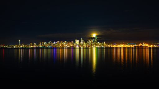 A wide angle shot of the city lights reflecting on the water under the moon