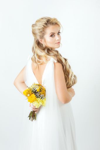 A vertical shot of a beautiful Caucasian bride in an elegant wedding dress posing on white background