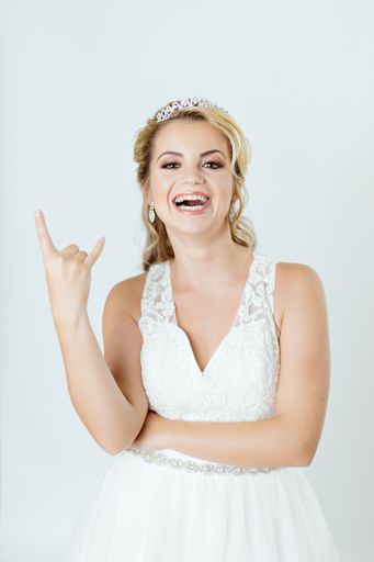 A vertical shot of a cheerful bride in a wedding dress doing funny poses and showing a rock gesture