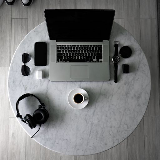 A top view of a cup of espresso on a table with a laptop and a phone with accessories on it