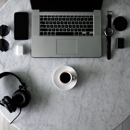 A top view of a cup of espresso on a table with a laptop and a phone with accessories on it