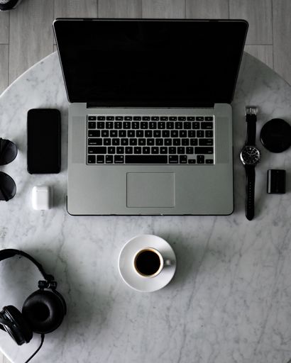 A top view of a cup of espresso on a table with a laptop and a phone with accessories on it
