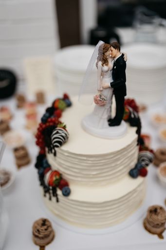 A wedding cake with a bride and groom topper, decorated with berries and chocolate, on a festive table setting.