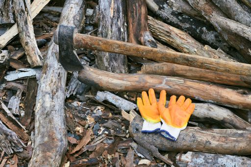 A scenic shot of a campsite filled with wooden planks, an ax, gloves, and burnt ashes
