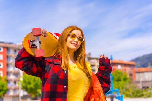A stylish redhead Hispanic lady enjoying a sunny day in an urban park holding her skateboard