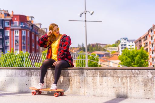 A stylish redhead Hispanic skater lady enjoying the sunny day sitting in an urban park