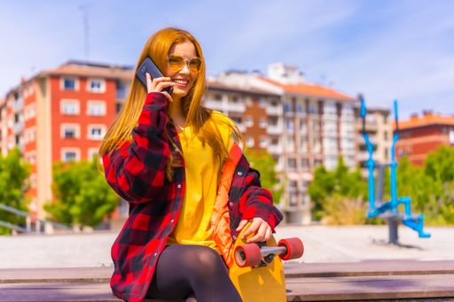 A stylish redhead Hispanic skater lady talking on her phone enjoying the sunny day in an urban park