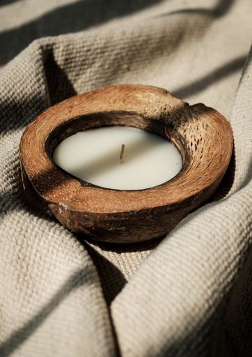 A vertical shot of a candle in a coconut on a pastel fabric.