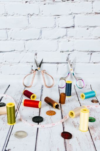 A vertical shot of accessories for needlework on a wooden table and brick wall background