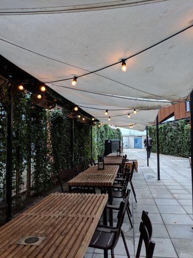 A vertical shot of wooden tables and chairs inside of a cafe with lights hanged on a ceiling