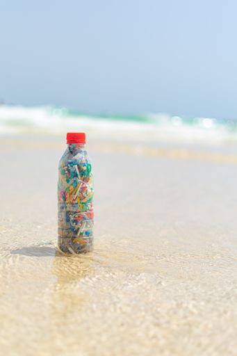 A vertical of a plastic bottle filled with collected microplastics on the sandy beach
