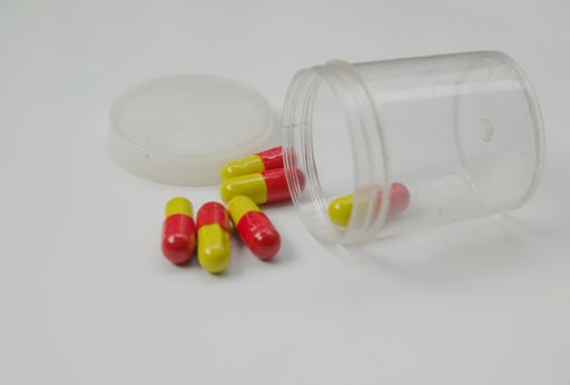 A transparent, plastic container of yellow, and red pill capsules with a white background