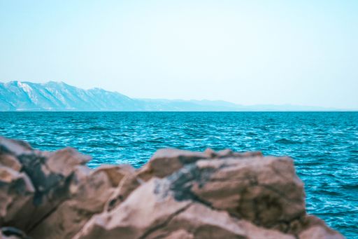 A beautiful view of a blue sea with a rocky coast on the background of mountains under a clear sky