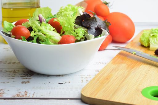 A selective focus shot of a vegetable salad on a ceramic plate and tomatoes in the background