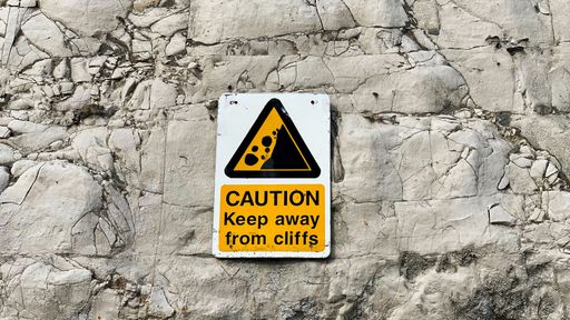 A yellow, triangle caution sign about rock slide attached to a cliff