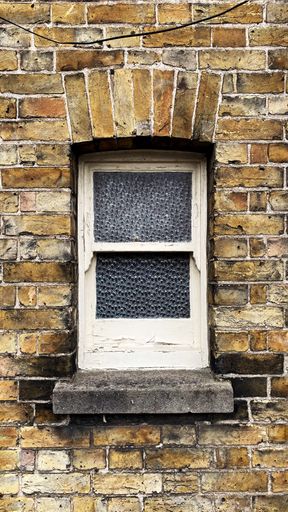 A vertical shot of a brick wall of a building and an old window in it
