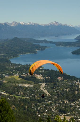 A paragliding flight scene over the city of Bariloche, with lake and mountains, in vertical with copy space