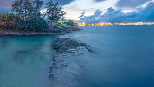A landscape view of a beautiful seashore surrounded by trees under a blue cloudy sky during the sunset
