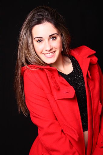 A portrait of a beautiful smiling Spanish wowearing a red coat against a black background