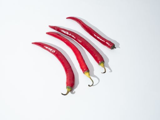 A top view of four red chili peppers on a white surface.