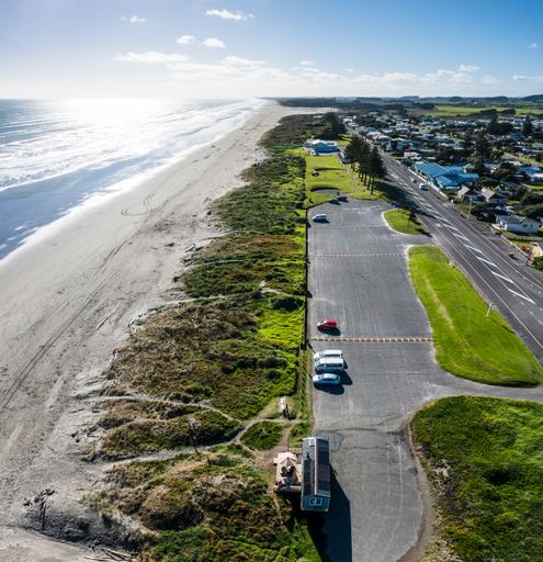 Long sandy beach, clear sky, parked cars, and homes by the Tasman Sea.