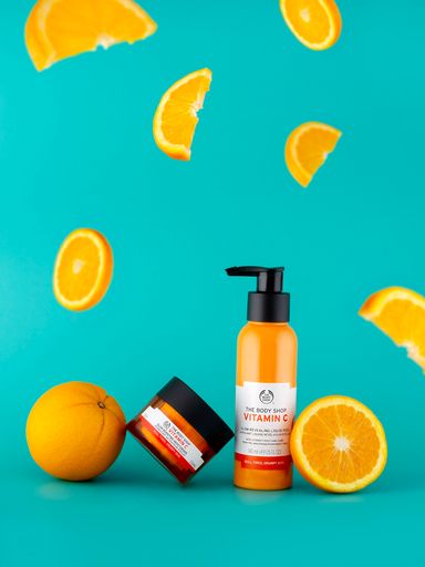 The Body Shop Vitamin C cosmetic set with flying oranges on a blue vertical background
