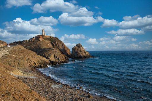 A Mesmerizing view of a beacon on a rocky cliff and sea water under a blue cloudy sky in cabo de gata Andalusia, Spain