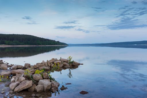 A shot of rocks in the sea with a reflection near hills during sunset