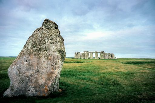 Stonehenge under a cloudy sky with a large stone in the foreground, showcasing the ancient monument and surrounding landscape.