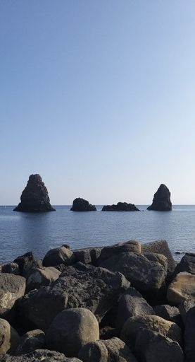 Scenic view of sea stacks in Aci Trezza, Sicily, against a clear blue sky, with rocky foreground.