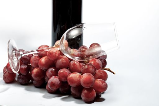 Bunch of red grapes with wine bottle and empty wineglass on white background, ready for a toast