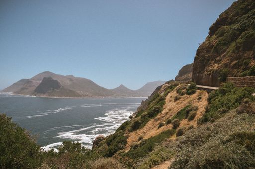 Scenic view of Chapman's Peak Drive along the coastline with mountains and ocean under a clear blue sky in Cape Town, South Africa.