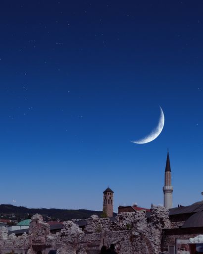 The waxing crescent on a blue sky over an ancient town