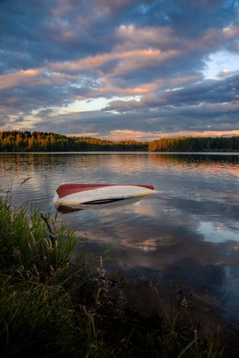 A vertical shot of an old weathered boat in a lake under the beautiful colorful sunset sky