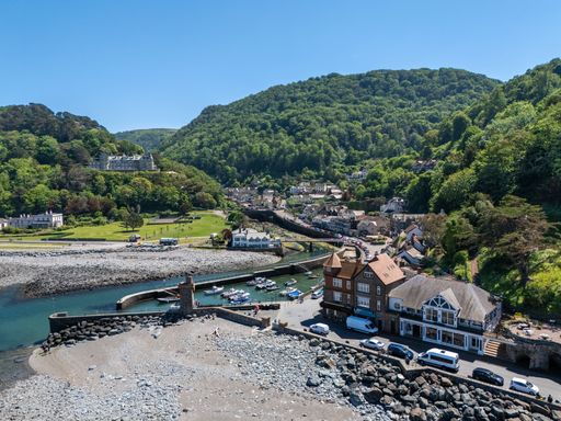 Aerial view of Lynmouth, a picturesque village in Devon, England, showing the harbor, lush green hills, and historic buildings on a sunny day.