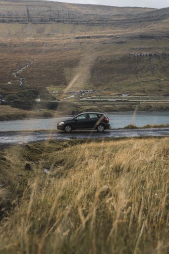 A vertical shot of a car driving on a road in nature, Faroe Islands
