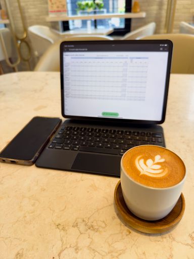 Cozy cafe setting with a tablet displaying a spreadsheet, a smartphone, and a cup of latte art.