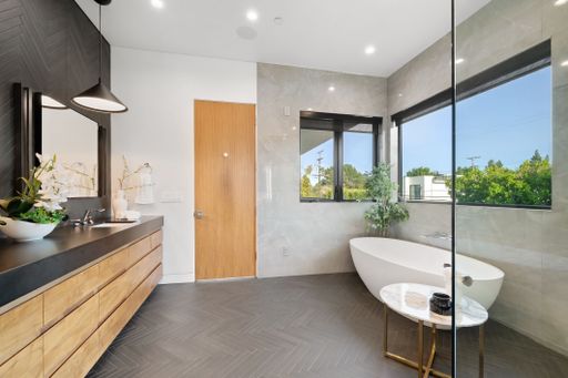 Elegant modern bathroom showcasing the freestanding tub, glass shower, pendant lights, and natural wood finishes.
