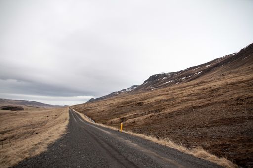 A beautiful view of the road in a field surrounded by hills on a cloudy day