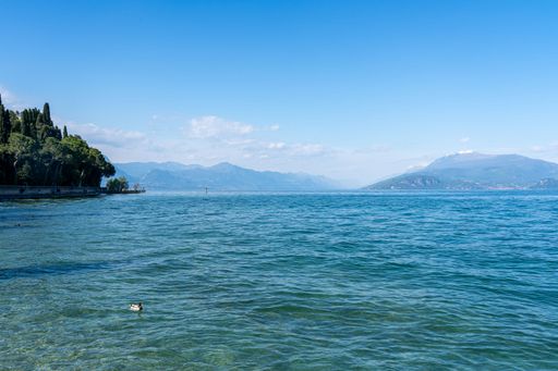Scenic view of Lake Garda with clear blue waters and distant mountains under a bright sky.