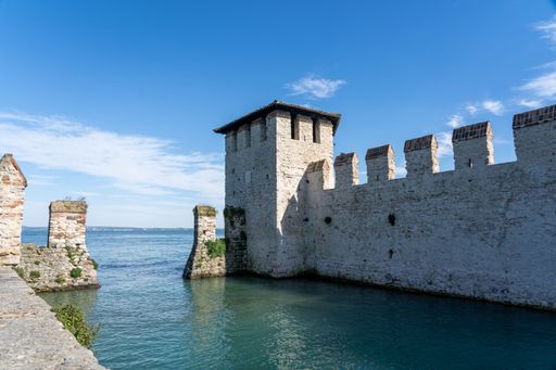 Scenic view of Scaliger Castle's stone walls and clear blue water under a bright sky in Sirmione, Italy.